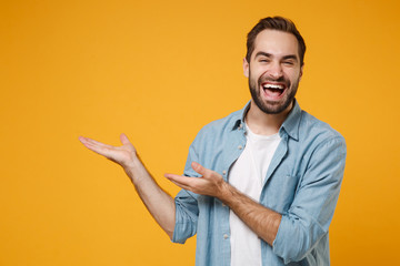 Laughing young bearded man in casual blue shirt posing isolated on yellow orange wall background,...