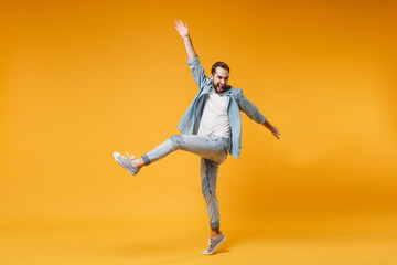 Funny young bearded man in casual blue shirt posing isolated on yellow orange wall background studio portrait. People emotions lifestyle concept. Mock up copy space. Jumping, spreading rising hands.