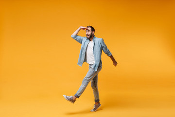Amazed young bearded man in casual blue shirt posing isolated on yellow orange background in studio. People lifestyle concept. Mock up copy space. Holding hand at forehead looking far away distance.