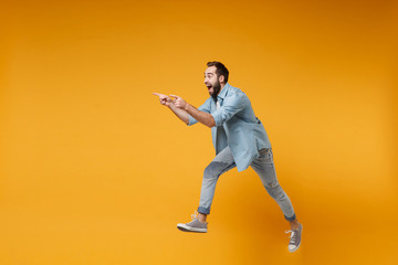 Excited young bearded man in casual blue shirt posing isolated on yellow orange background studio portrait. People emotions lifestyle concept. Mock up copy space. Jumping pointing index fingers aside.