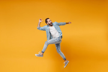 Side view of cheerful young bearded man in casual blue shirt posing isolated on yellow orange background, studio portrait. People emotions lifestyle concept. Mock up copy space. Jumping looking back.