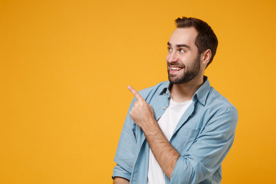 Smiling young bearded man in casual blue shirt posing isolated on yellow orange background studio portrait. People sincere emotions lifestyle concept. Mock up copy space. Pointing index finger up.