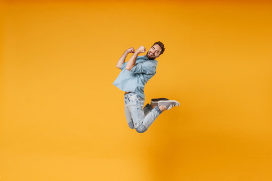 Happy young bearded man in casual blue shirt posing isolated on yellow orange background, studio portrait. People sincere emotions lifestyle concept. Mock up copy space. Jumping doing winner gesture.
