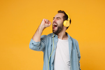 Young man in casual blue shirt posing isolated on yellow orange wall background studio portrait. People sincere emotions lifestyle concept. Mock up copy space. Listen music with headphones, sing song.