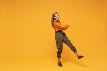 Fototapeta na wymiar Cheerful little blonde kid girl 12-13 years old in turtleneck, jumpsuit isolated on orange yellow background children studio portrait. Childhood lifestyle concept. Mock up copy space. Looking camera.