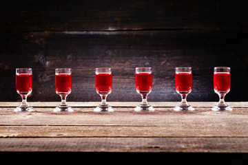 Set of alcoholic cherry cocktails in shot glasses on old wooden plank. Rustic background with vodka in shooters.