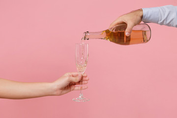 Close up cropped photo of female, male hold in hands bottle glass of champagne isolated on pink...