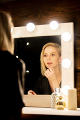 blonde woman in dress near makeup mirror