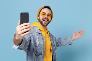 Smiling young hipster guy in fashion jeans denim clothes isolated on pastel blue wall background....