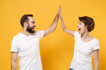 Laughing young couple friends bearded guy girl in white blank empty t-shirts isolated on yellow...