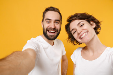 Close up of cheerful young couple friends bearded guy girl in white t-shirts isolated on yellow orange wall background. People lifestyle concept. Mock up copy space. Doing selfie shot on mobile phone.