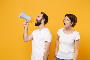 Bewildered young couple friends bearded guy girl in white blank empty t-shirts isolated on yellow orange background. People lifestyle concept. Mock up copy space. Scream in megaphone, looking aside.