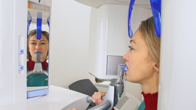 Doctor to take a image 3d scanner tomography of teeth and jaw in modern laboratory dental clinic. Female nurse shows the patient woman an x-ray machine 3d digital scanner. Computer dental diagnostics.