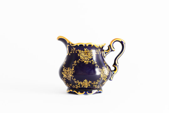 Closeup of a beautiful cobalt blue colored vintage porcelain tea milk jug with golden floral pattern on white background