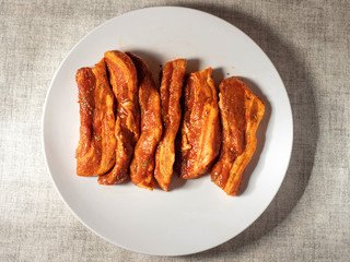 Korean style marinated pork belly slices, close up, on a white plate. Fresh meat preparation.