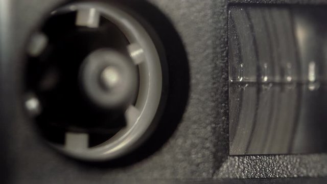 Macro shot of audio cassette reel with a magnetic tape rotating in the tape recorder during the playback. Concept of playing music, recording a conversation, listening sounds. 4K resolution video.