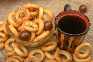 Small bagels, chocolates, a mug of tea and a rough homespun cloth on a wooden background close-up.