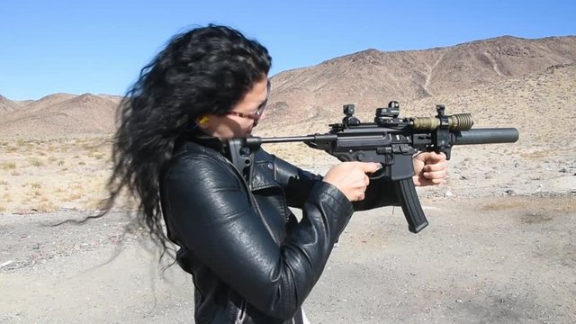 Brunette woman firing a rifle at a metal target at a desert shooting range.