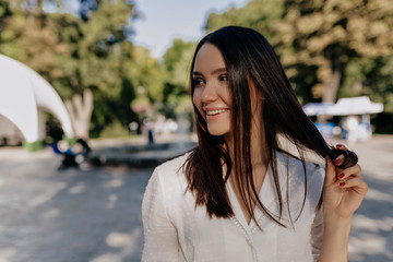 Fototapeta premium Romantic pretty woman with dark hair playing with her hair and looking aside with shy smile