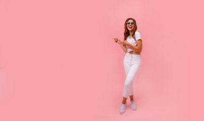 Fototapeta na wymiar Image of happy young lady standing isolated over pink background. Looking camera pointing.Photo of happy young woman standing isolated over pink wall background, showing copyspace.