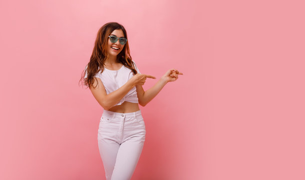 Full length Image of happy young lady standing isolated over pink background. Looking camera pointing.Photo of happy young woman standing isolated over pink wall background, showing copyspace.