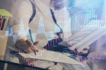 A woman hands writing information about stock market in notepad. Forex chart holograms in front. Concept of research.