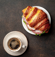coffee and croissant - a sandwich with sausage and cheese on a cutting board on a stone background 
