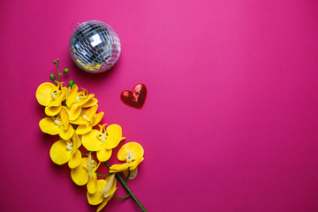 Yellow orchids, disco ball and red heart with sequins on pink background with copy space. Saint Valentine's day card on pink background.