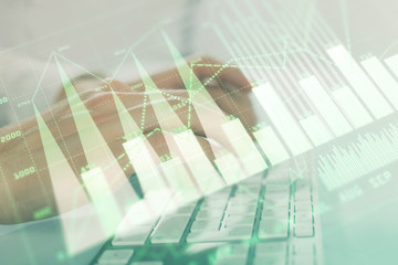 Double exposure of graph with man typing on computer in office on background. Concept of hard work. Closeup.