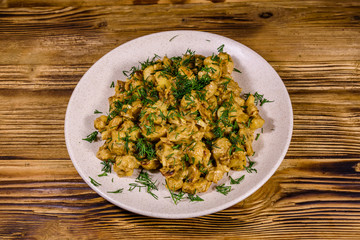 Plate with champignons stewed in sour cream on a wooden table