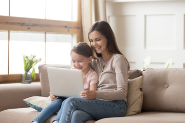 Happy mother and preschool daughter using laptop together at home