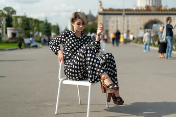 female lifestyle lessons posing on a chair outdoors on a summer day. effective European model in a...