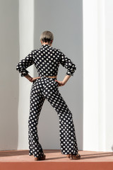 Fototapeta premium beautiful caucasian girl in a black pantsuit with white spots, pants and a shirt, high heel. Short haircut, bright makeup. Cool Posing at a white building with columns