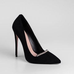 Womens black suede high-heeled shoes with a decorative strap element with shiny rhinestones on toe. Close-up. On a white background for a catalog