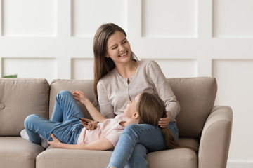 Fototapeta premium Little daughter lying on happy mother knees, having fun together
