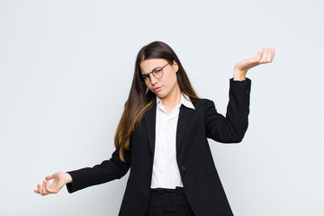 young businesswoman shrugging with a dumb, crazy, confused, puzzled expression, feeling annoyed and...