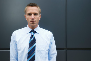 Portrait of a serious businessman standing against dark modern wall looking at the camera with a blank expression