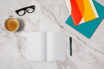 Opened notebook with pen and other colorful stationery, mug of coffee and classical glasses on marble background 
