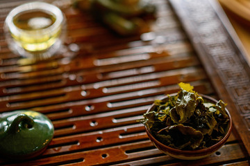 Brewed leaves of Chinese oolong tea in a cup on a tea wooden board. Tea ceremony. Soft focus.