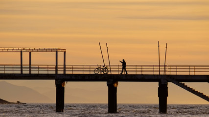 Silhouette of walking man and bike on the pier