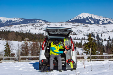 man sitting in car trunk changing for snowboard
