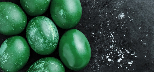Greeting card with easter eggs painted in green grass shiny dye color on black background with white crumbs, egg shell with white stains, scuffs, scratches. handmade Flat lay with copy space