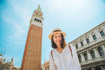 Fototapeta na wymiar smiling pretty caucasian woman rise up hands at venice city square bell tower on background