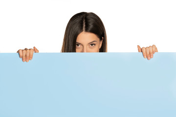 Fototapeta premium young beautiful woman peeking behind a blue empty board