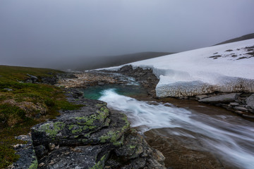 Beautiful bleak summer landscape of tundra with the river and snow in foggy morning, Norway