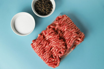 Raw ground beef, salt and black pepper on blue background. Food preparation concept, ingredients...
