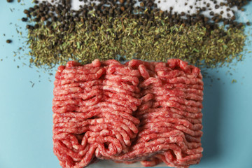 Raw ground beef, salt, black pepper and dry herbs on blue background. Food preparation concept, ingredients for burger, cutlet or meatball. Top view, flat lay