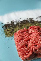 Raw ground beef, salt, black pepper and dry herbs on blue background. Food preparation concept, ingredients for burger, cutlet or meatball. Top view, flat lay