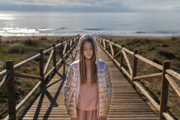 teen on the beach with hood on wooden walkway