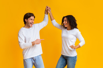 Affectionate interracial couple holding hands and dancing together over yellow background
